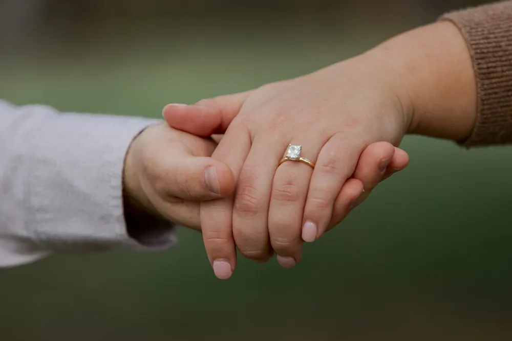 Two hands held together, an engagement ring on hers