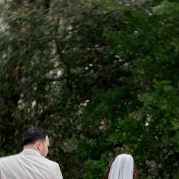 A bride in a long veil walking up behind the groom for their first look