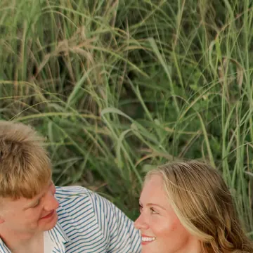 A smiling couple sitting close together in tall beach grass