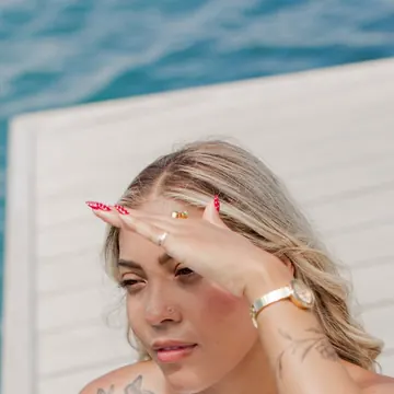A woman shading her eyes in the sun beside a white boat railing over blue water