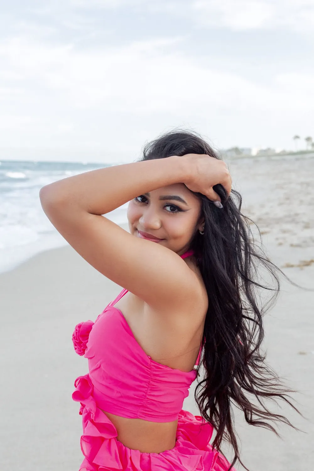 A woman in pink with windblown hair on the beach