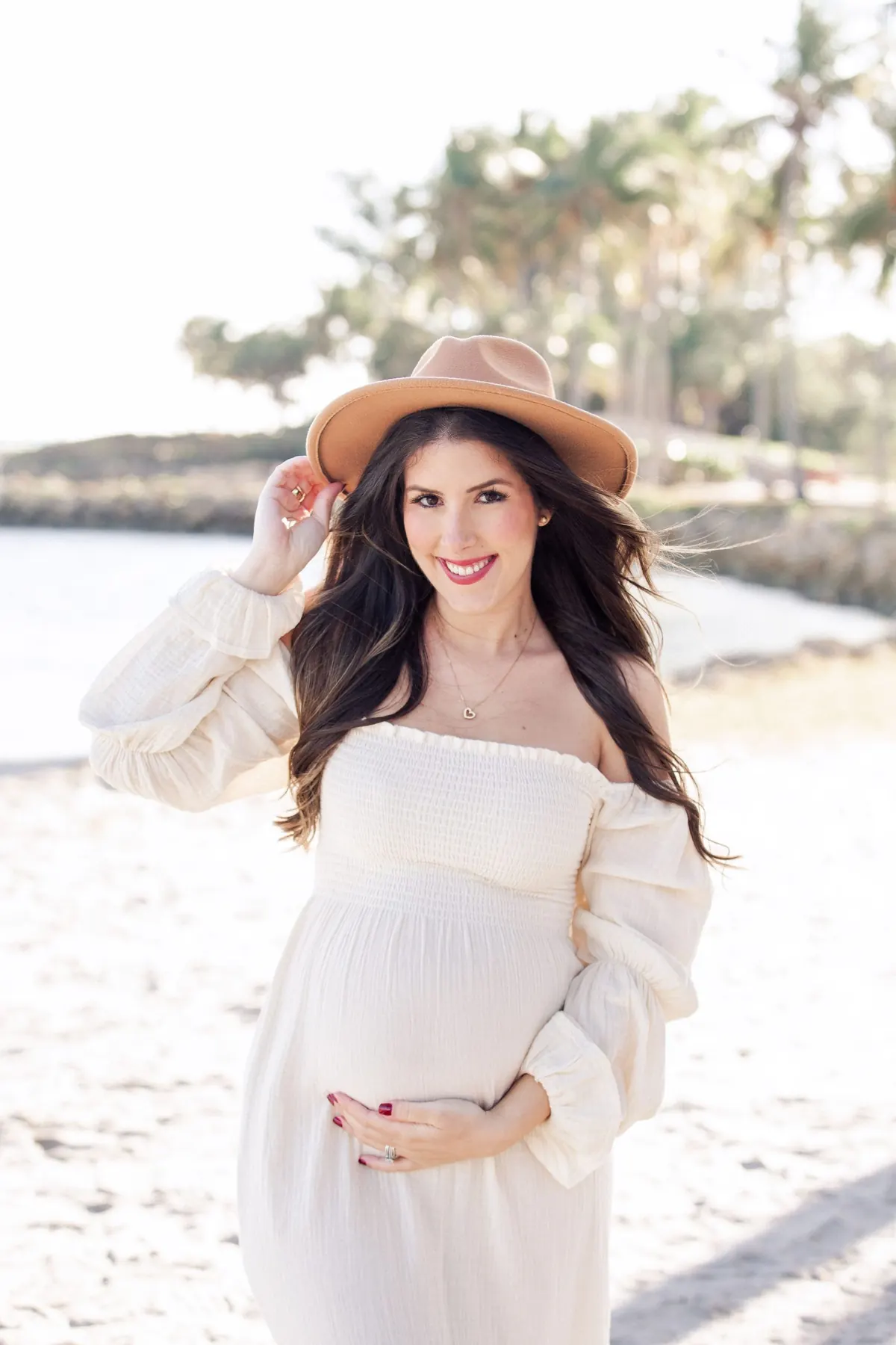 Expecting mom in a white dress and hat on the beach