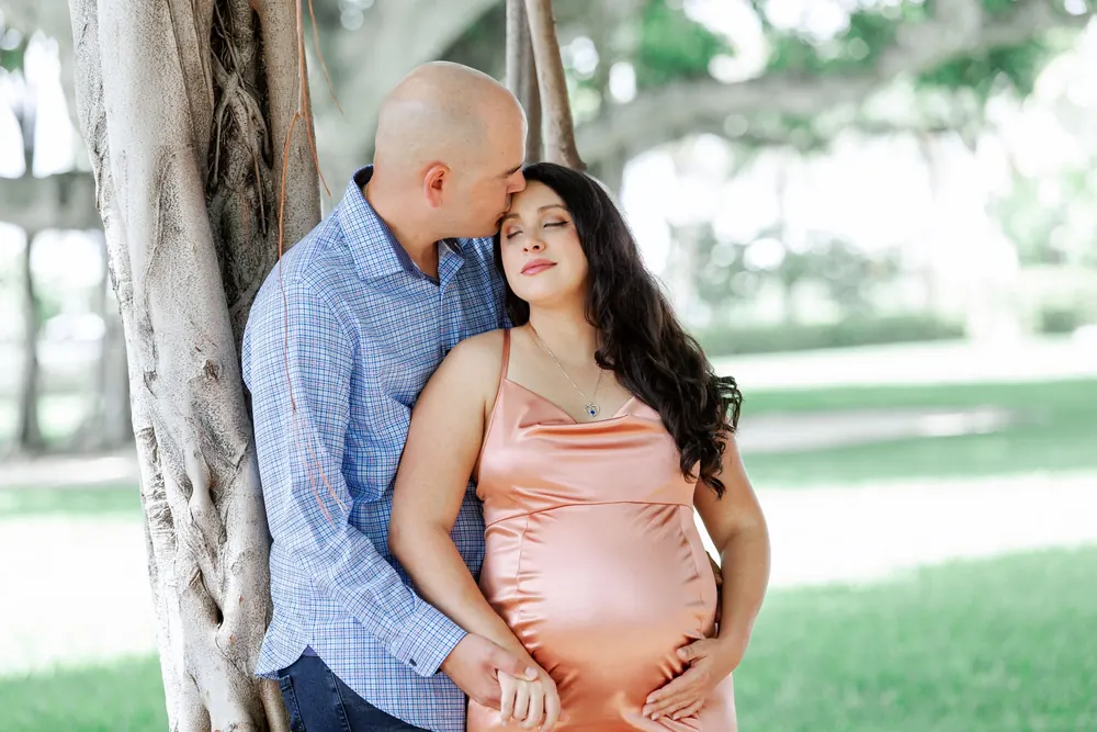 An expecting couple under an oak tree, her hand on the bump