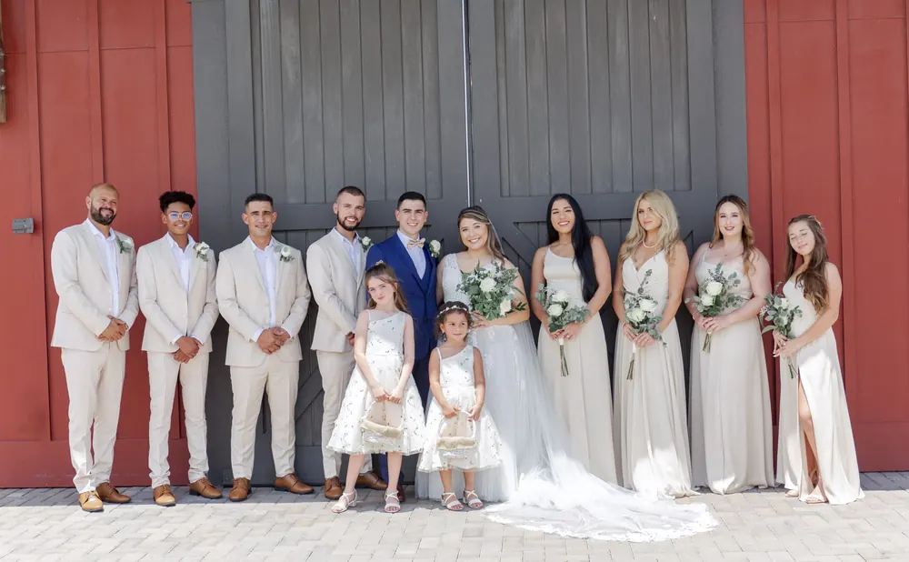 Bride, groom and the wedding party lined up in front of a red barn wall